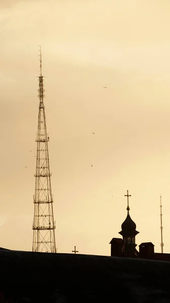 farklı çağlardan kuleler, altın güneş ışınlarının arka planında siluetler, kilisenin haçı ve radyo televizyon kulesi, şehir manzarası, sakinlik ve sessizlik, iyi hava ve atmosfer, turuncu gökyüzü