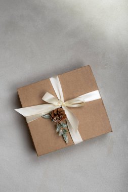 Beyaz kurdeleli renkli Noel hediyesi kutusu ve gri arka planda çam kozalağı.