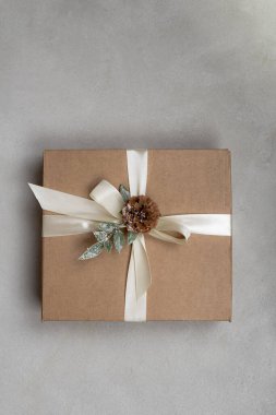 Beyaz kurdeleli renkli Noel hediyesi kutusu ve gri arka planda çam kozalağı.