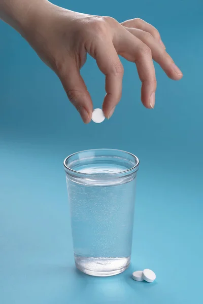 Glass of water and vitamins, pills and tablets. Light blue background. Female hand throws a pill.