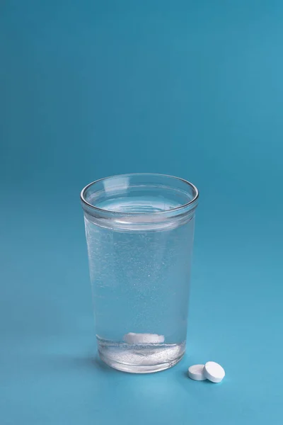 Glass of water and vitamins, pills and tablets. Light blue vertical background. Place for text.