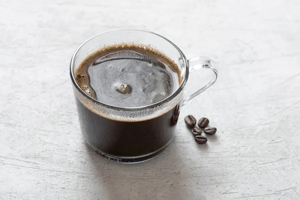 薄い背景に透明なマグカップの中のブラックコーヒー — ストック写真