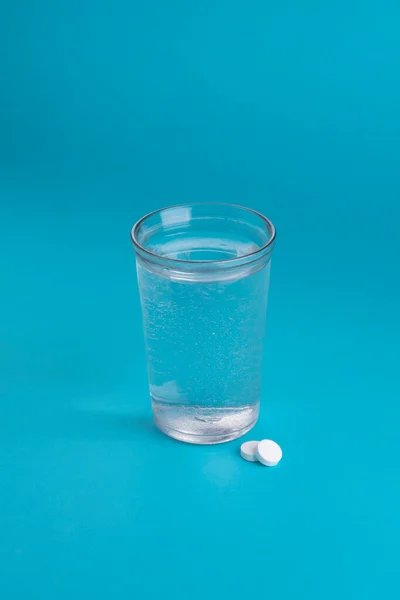 Glass of water and vitamins, pills and tablets. Light blue vertical background.