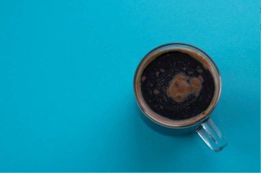 Mavi arka planda köpüklü bir bardak espresso kahvesi. Metin için yer.
