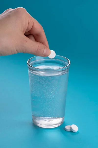 Glass of water and vitamins, pills and tablets. Light blue vertical background.