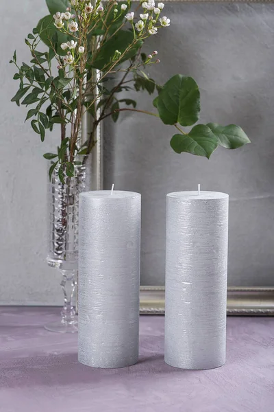 Silver candles with a green branch and a silver frame on a gray background, close-up.