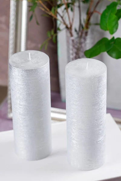 Silver candles with a green branch and a silver frame on a vertical gray background, close-up.