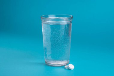 Bir bardak su, vitamin, hap ve tablet. Açık mavi arkaplan.