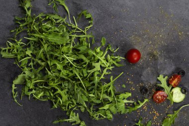 Taze sebzeler, roka, domates, salatalık, otlar, biberler ve koyu gri dokulu arka planda zeytinler. Yukarıdan görüntüle.