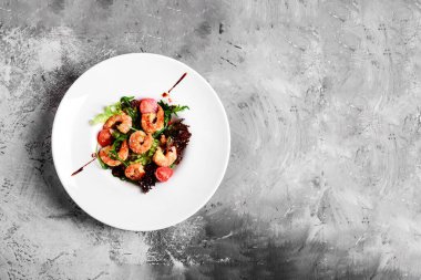 Beyaz tabakta kral karidesli yeşil salata, sağlıklı yemek konsepti. Açık gri arkaplan. Metin ve metin boşluğu için boşluk.