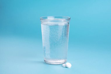 Bir bardak su, vitamin, hap ve tablet. Açık mavi arkaplan.