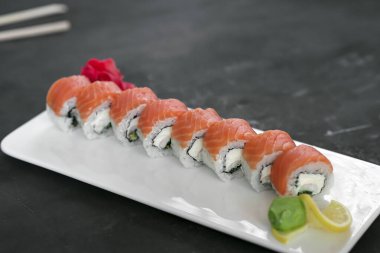 Japon suşisi yakın plan. Beyaz plaka üzerinde yan görünüm, koyu gri yatay arkaplan.