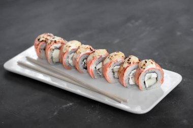 Japon suşisi yakın plan. Beyaz plaka üzerinde yan görünüm, koyu gri yatay arkaplan.