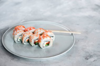 Japon suşisi yakın plan. Beyaz bir plakanın yan görünümü, açık gri desenli arkaplan.