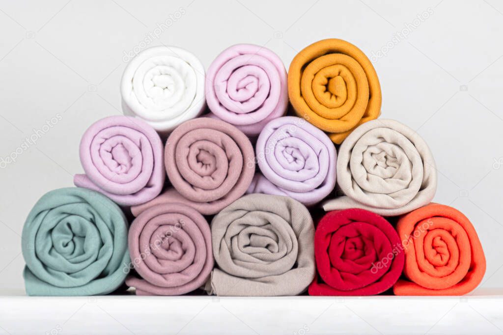 Rolls of knitted fabric of different shades, lilac, purple, gray, red, white close-up, on a gray background