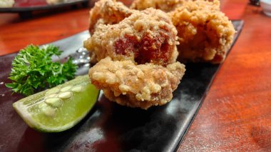 Kızarmış Japon usulü kızarmış tavuk, taze limon ve siyah tabakta maydanozla servis ediliyor.