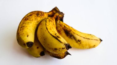 Beyaz arka planda kahverengi benekli olgun sarı muzlar.