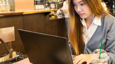 Bir kahve dükkanında bir dizüstü bilgisayar üzerinde çalışan Asyalı kadın öğrenci