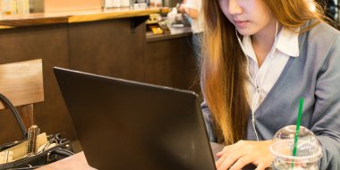 Bir kahve dükkanında bir dizüstü bilgisayar üzerinde çalışan Asyalı kadın öğrenci