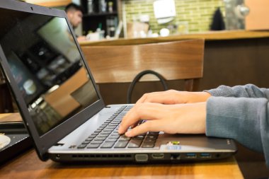 Bir kahve dükkanında bir dizüstü bilgisayar üzerinde çalışan Asyalı kadın öğrenci el