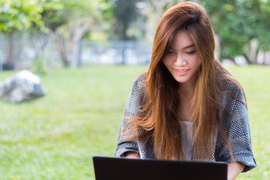 Bir bahçe veya park bir dizüstü bilgisayarda çalışan gülümseyen Asyalı kadın