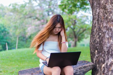 Bir bahçe veya park bir dizüstü bilgisayar üzerinde çalışan Asyalı kadın