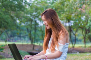 Bir bahçe veya park gülümseyen bir dizüstü bilgisayar üzerinde çalışan Asyalı kadın