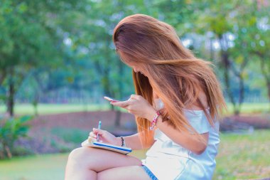 Kitap yazma ve smartphone parkta oynarken Asyalı kadın