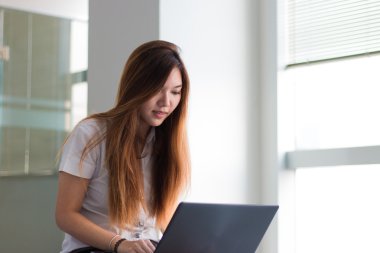 Asyalı öğrenci yakın bir binada gülümseyen bir dizüstü bilgisayar üzerinde çalışan