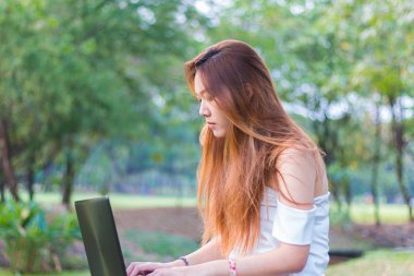 Bir bahçe veya park bir dizüstü bilgisayar üzerinde çalışan Asyalı kadın