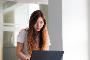 Asyalı öğrenci pencere yakın bir binada bir dizüstü bilgisayar üzerinde çalışan