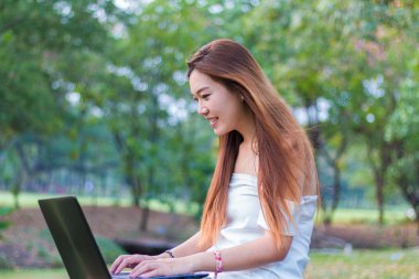Bir bahçe veya park gülümseyen bir dizüstü bilgisayar üzerinde çalışan Asyalı kadın