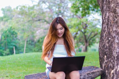 Bir bahçe veya park gülümseyen bir dizüstü bilgisayar üzerinde çalışan Asyalı kadın