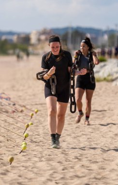 İki kararlı lezbiyen bayan sporcu sahilde engelli bir pistte ağır zincirler taşıyarak eğleniyorlar..