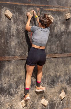 Engelli bir pistte tahta tutarak dikey duvara tırmanan güçlü bir bayan sporcunun arkasından bakın..