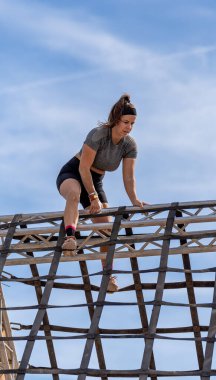 Kararlı, odaklanmış ve dengeli bir bayan sporcu dik, piramit şeklinde bir engelin zirvesini, mavi gökyüzünün arka planına karşı fethediyor..
