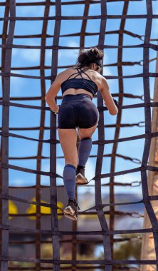 İnce, koyu renk saçlı bir bayan sporcu aşırı bir yarış sırasında dikey bir engel ağından iniyor..