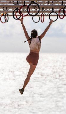 İnce bir dişi atlet, kristal berrak, ışıl ışıl okyanus suyuyla iskeleye asılmış birkaç halkanın üzerinde zıplıyor ve sallanıyor..