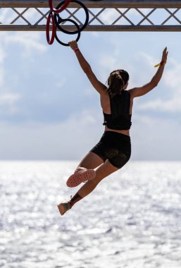 Bir halkayı tamamlarken dengede duran genç bir bayan sporcunun arka planda parlak bir gökyüzü olan denizin üzerinde duran engelini görüyor..