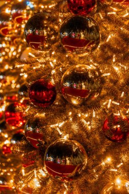 Parlak altın ve kırmızı top süsleri ve sıcak beyaz ışıklarla süslenmiş bir Noel ağacının yakın çekimi..