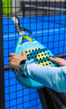 Saha çitlerine yaslanmış bir raket tutan bayan sporcunun elleri yakın plan..