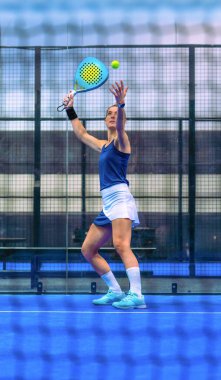 Padel oynayan atletik bir kadının ağıyla ön manzara, kapalı bir kortta ya ezer ya da hizmet eder..