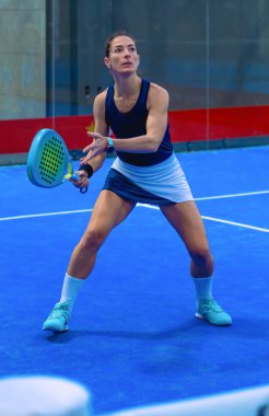 Kararlı bir dişi Padel oyuncusu, güçlü bir forehand 'ın hemen öncesinde, gözleri kapalı bir sahada yaklaşan topa kilitlenir..