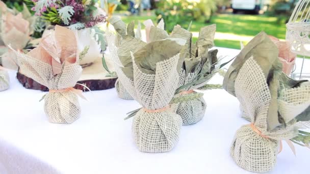 Plusieurs petits cadeaux emballés dans des sacs en toile de jute sont sur la table. Décoration de mariage — Video