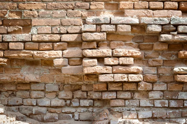 crumbling old brick wall of a building made of red brick, part of the wall is subject to destruction and damage. The wall of the fort and defensive structure with loopholes. History and culture.