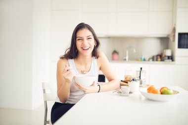 Young smiling woman eating cereal and smiling.Healthy breakfast.Starting your day.Dieting,fitness and wellbeing.Positive energy and emotion.Productivity,happiness,enjoyment concept.