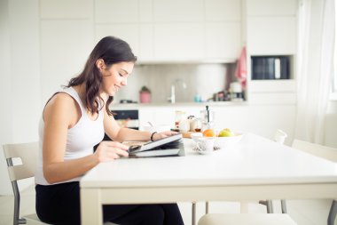 Young brunette is reading the newspaper while having breakfast at home.Modern woman lifestyle-healthy fitness breakfast,coffee and fruit,reading motivational quotes