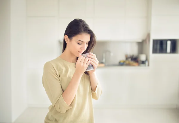 Young woman enjoying,holding cup of hot beverage,coffee or tea in morning sunlight.Enjoying her morning coffee in the kitchen.Savoring a cup of coffee breathing in the aroma — Stock Photo, Image