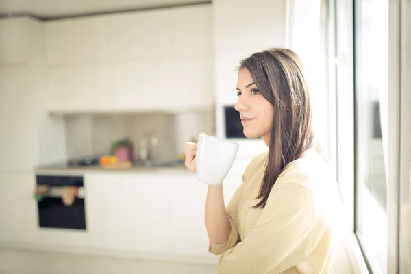 Young woman enjoying,holding cup of hot beverage,coffee or tea in morning sunlight.Enjoying her morning coffee in the kitchen — Stockfoto