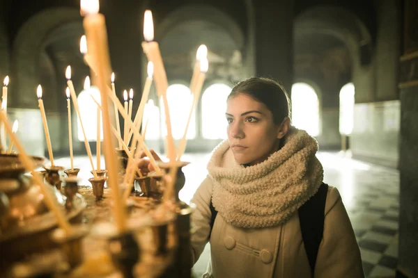 Young female lighting candles in a church during praying.Yellow votive candles burning.Woman praying to god at St. Alexander Nevsky Cathedral — Stock Photo, Image